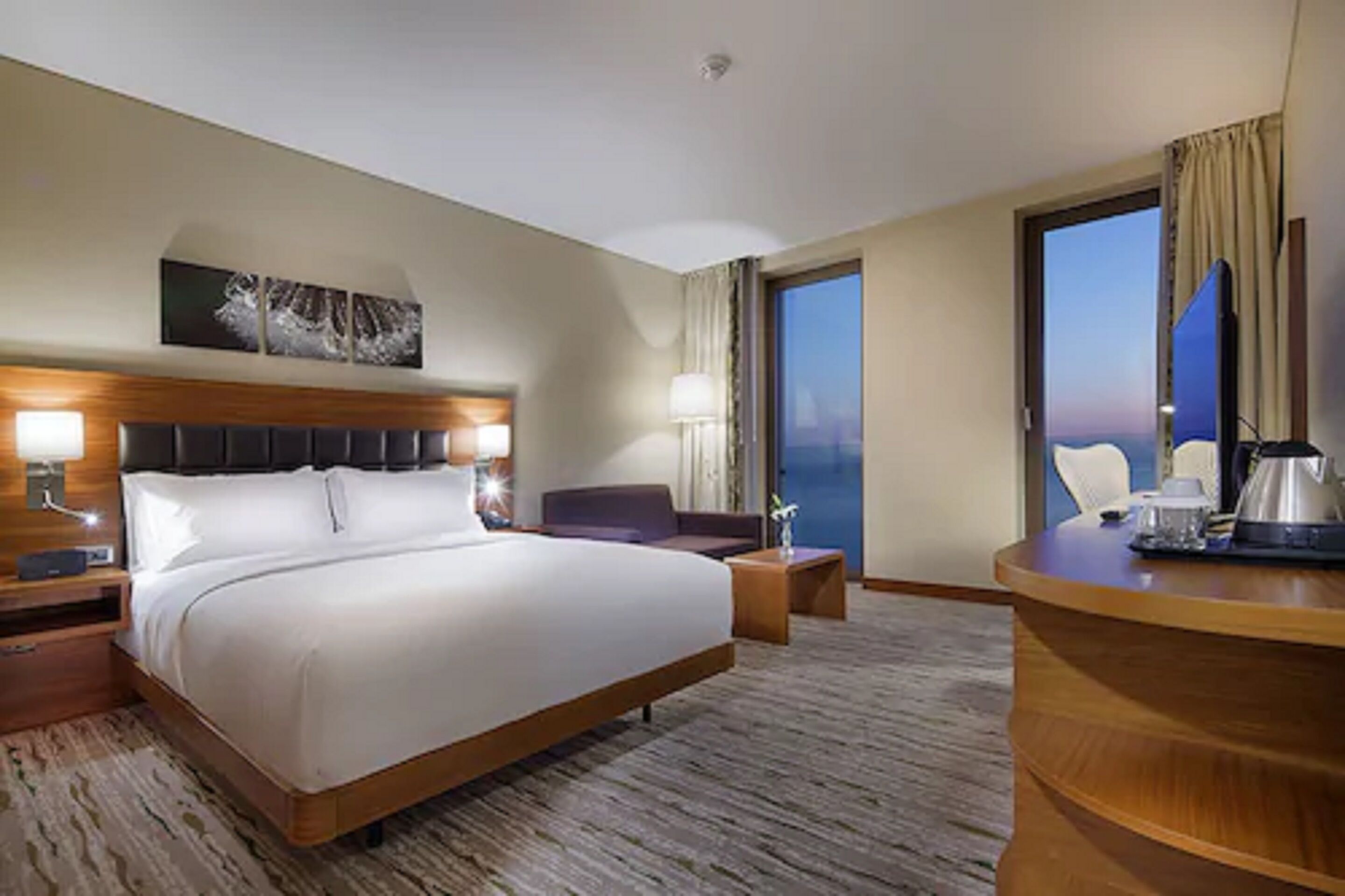 Une chambre d’hôtel avec un grand lit, un bureau avec une chaise, un canapé et une vue sur le paysage urbain.