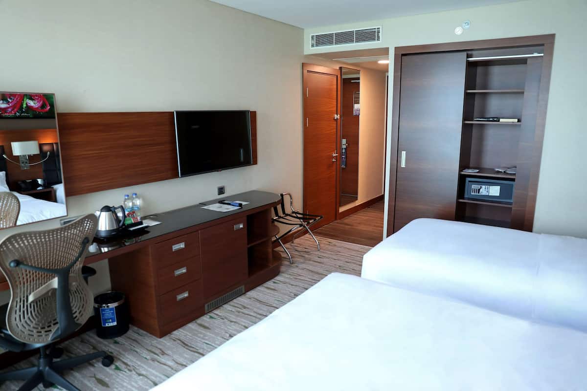Quarto de hotel com cama, secretária com cadeira, televisão, guarda-roupa e uma pequena cozinha.