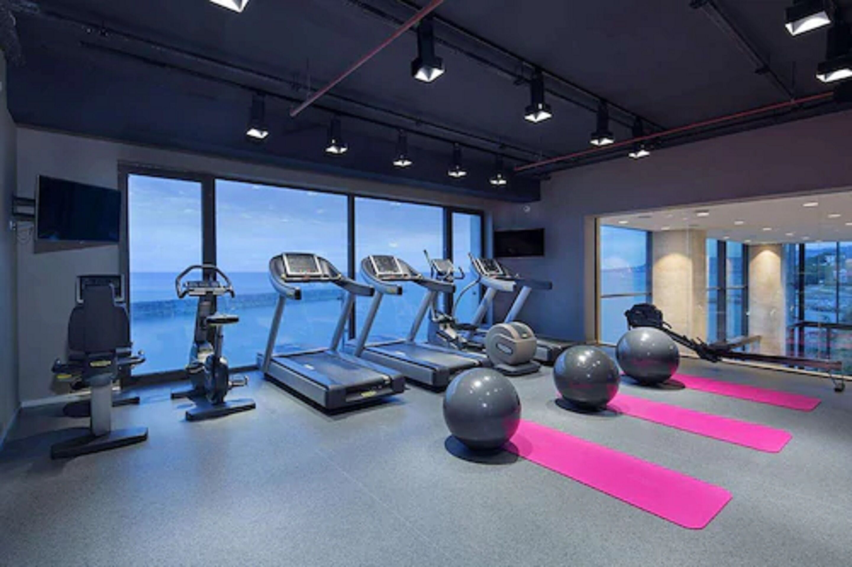 Une salle de sport équipée de tapis de course, de ballons d’exercice et de tapis roses.