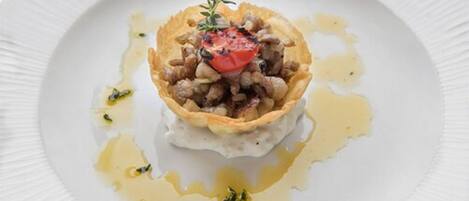 Un plato con base crujiente, cubierto de tomate y hierbas, servido en una placa blanca con borde texturizado.