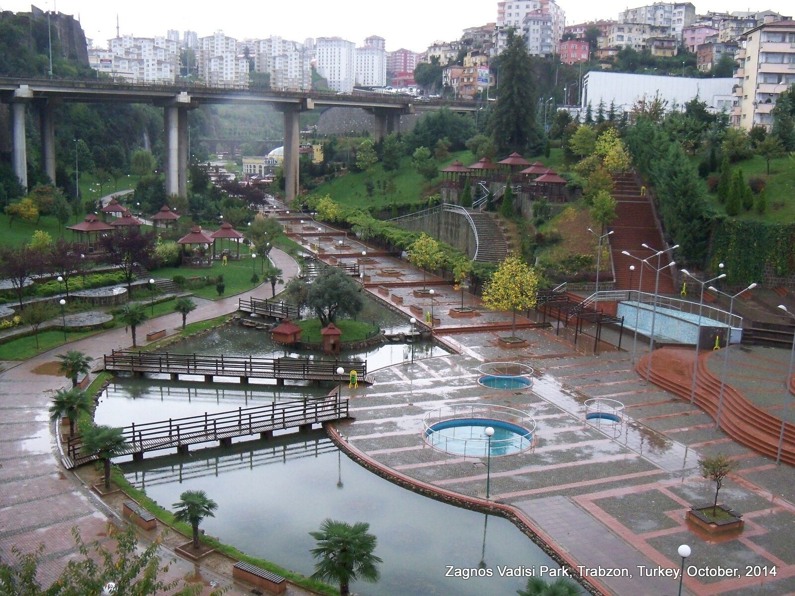 A park with a bridge, water features, and a view of the cityscape in Trabzon, Turkey.