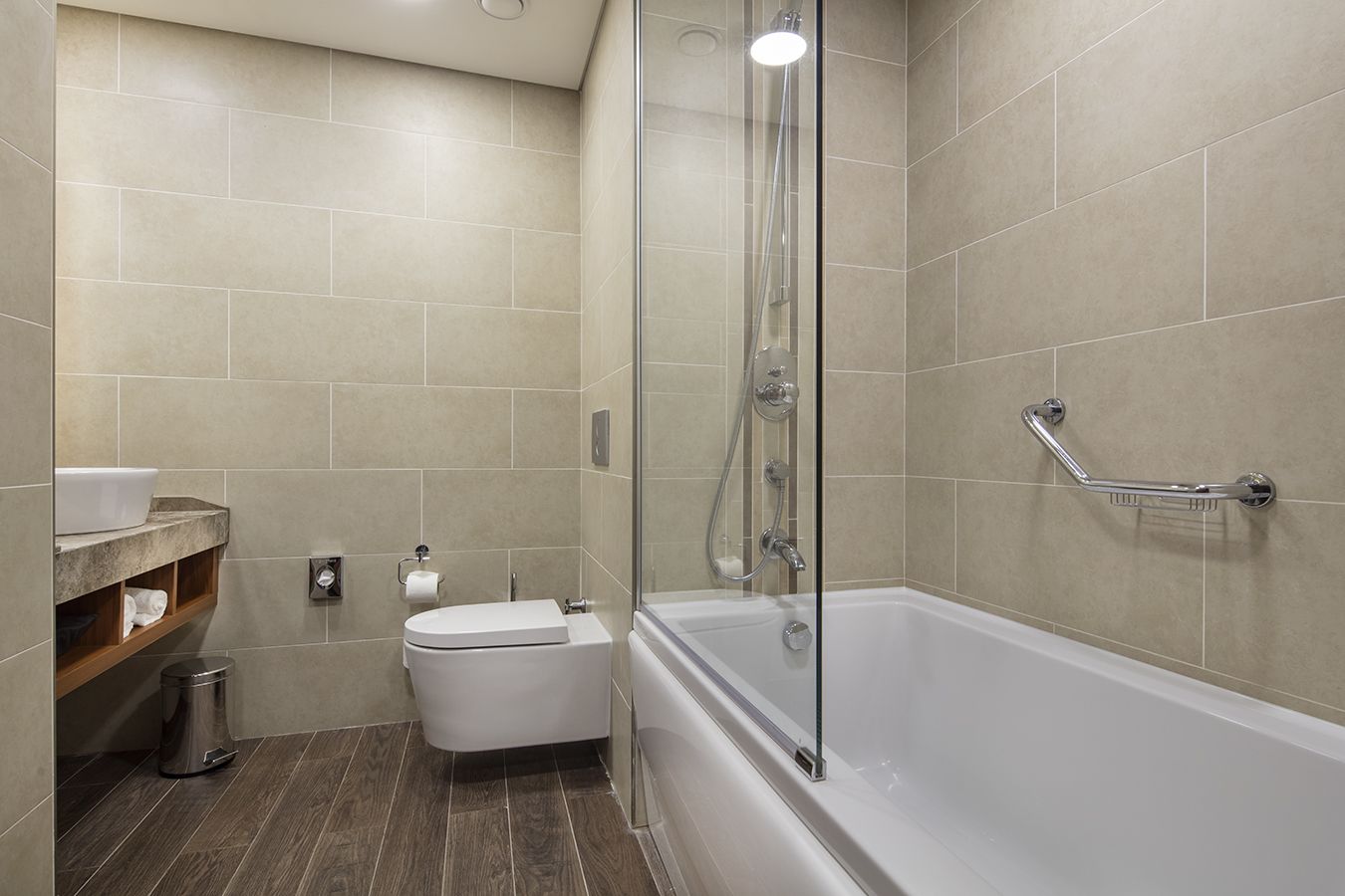 A modern bathroom with a glass-enclosed shower, a white bathtub, and a toilet.