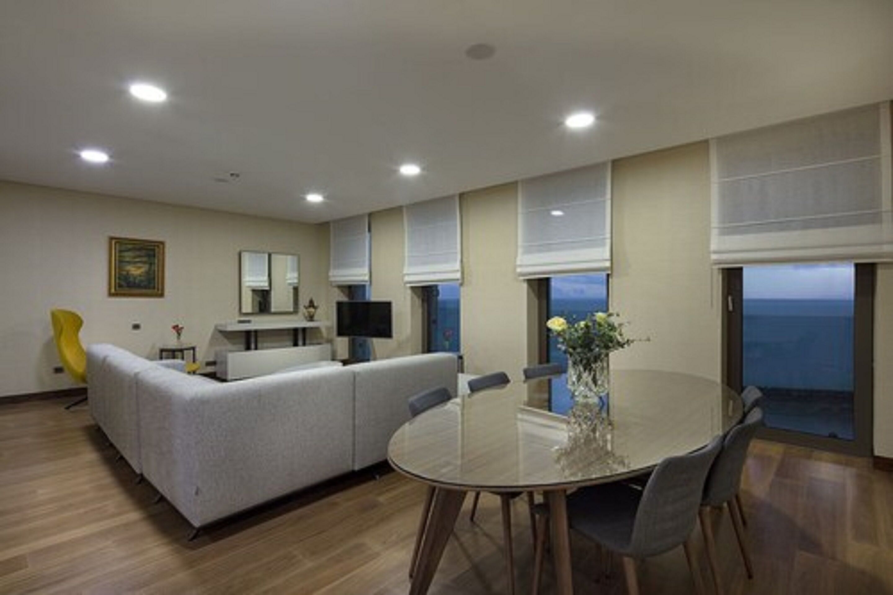 A modern living room with a sofa, a dining table with chairs, a TV, and a view of the ocean.