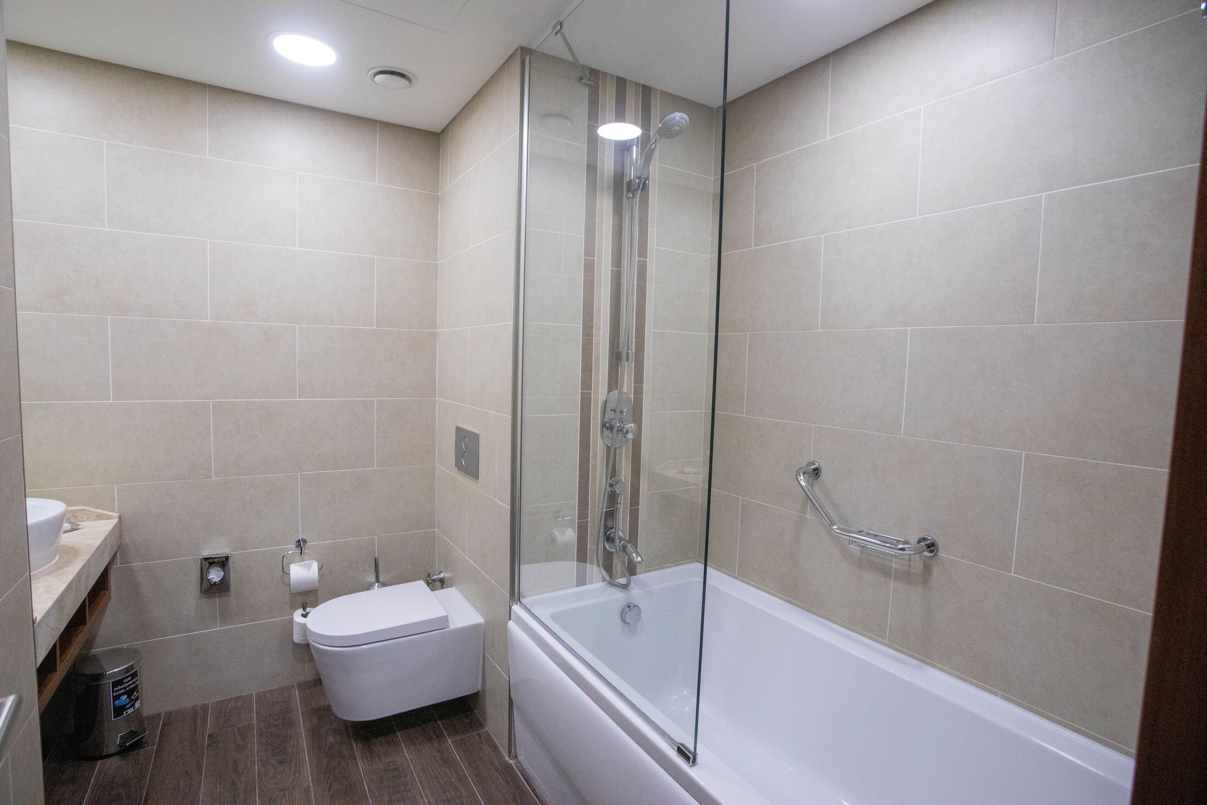 A modern bathroom with a glass-enclosed shower, a white bathtub, and a toilet.