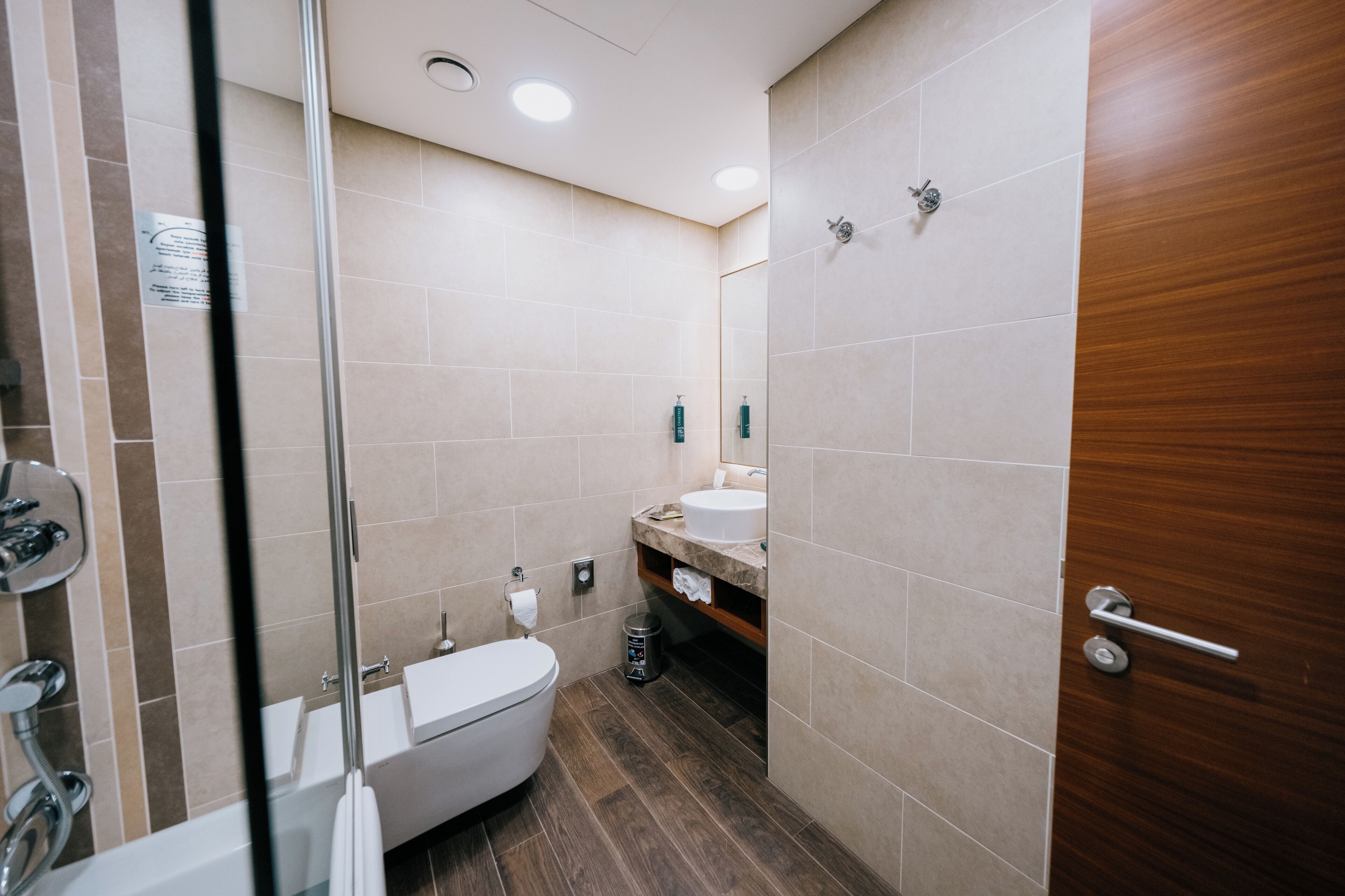 Ein modernes Badezimmer mit Duschkabine aus Glas, einer weißen Toilette und einer Holztür.