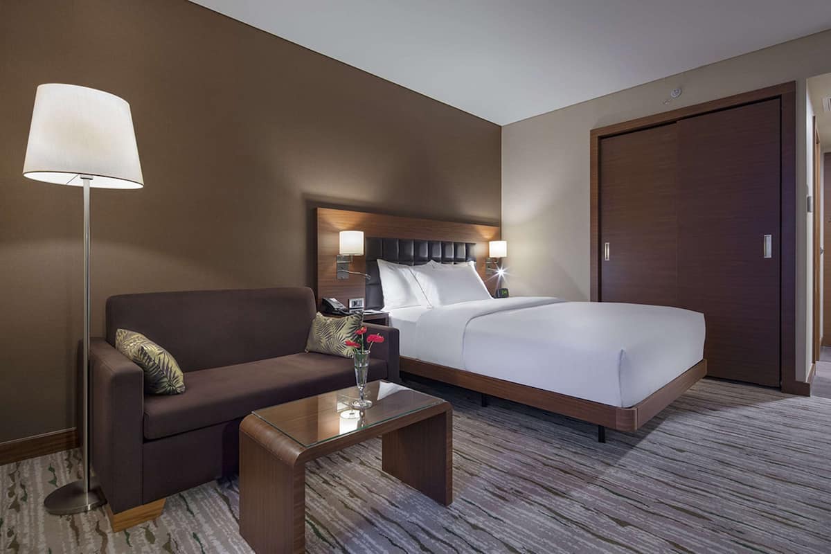 Quarto de hotel com cama, sofá, mesa de centro e luminária.