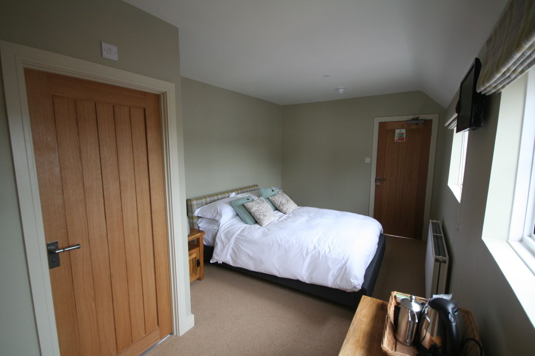 A bedroom with a wooden door, a bed with white bedding, a bedside table, and a radiator.