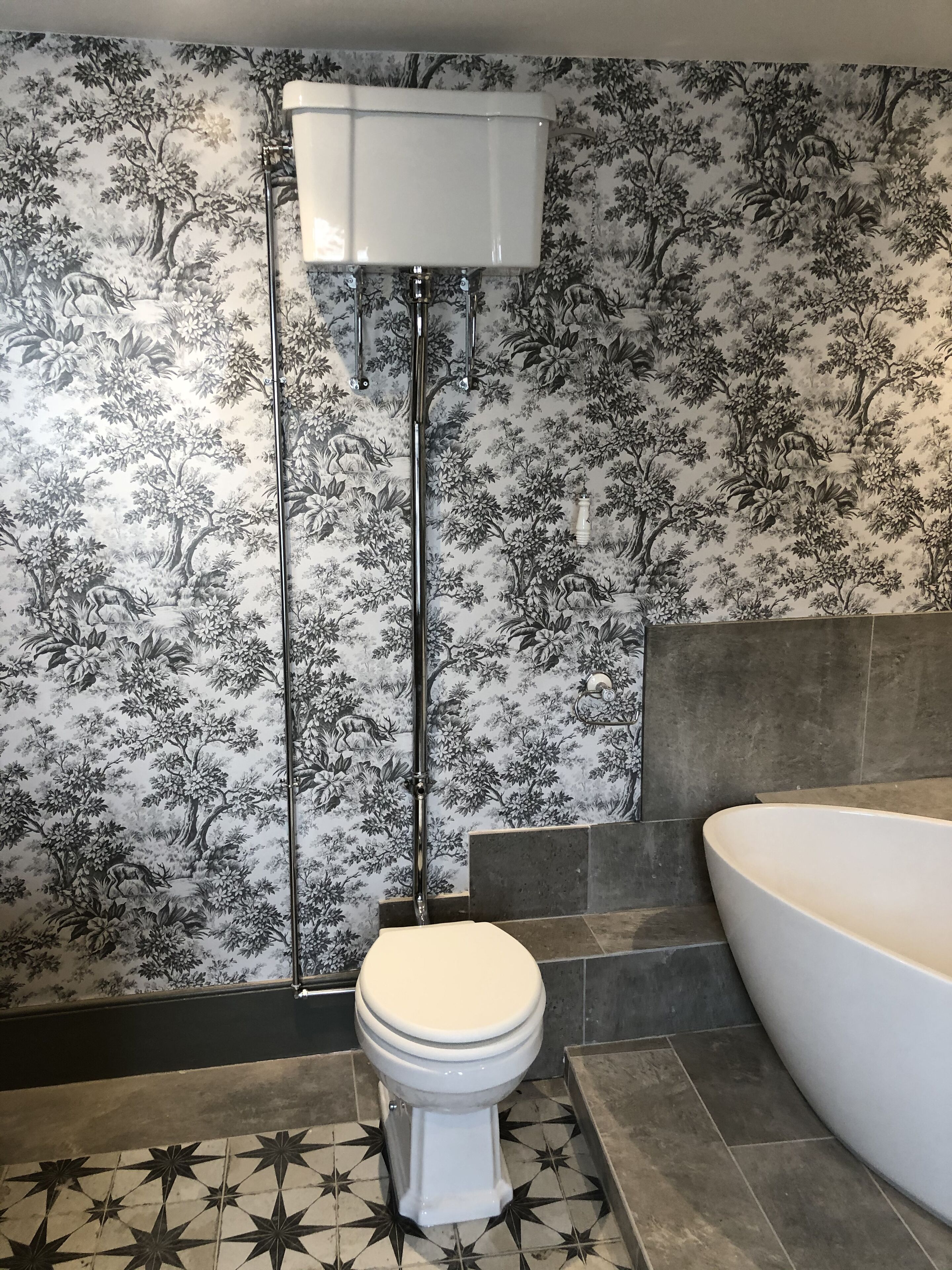 Ett badrum med toalett, badkar och en vägg med blommig tapet.