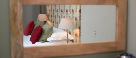 A bedroom with a bed, pillows, a nightstand, and a mirror reflecting the room.