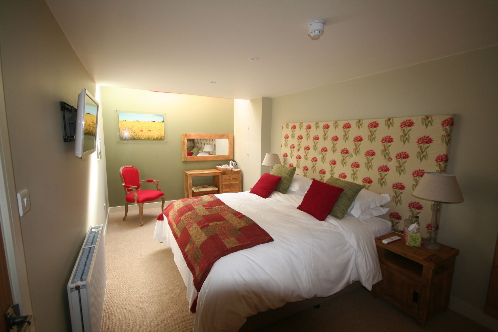A bedroom with a bed, bedside tables, a chair, a desk, and a radiator.