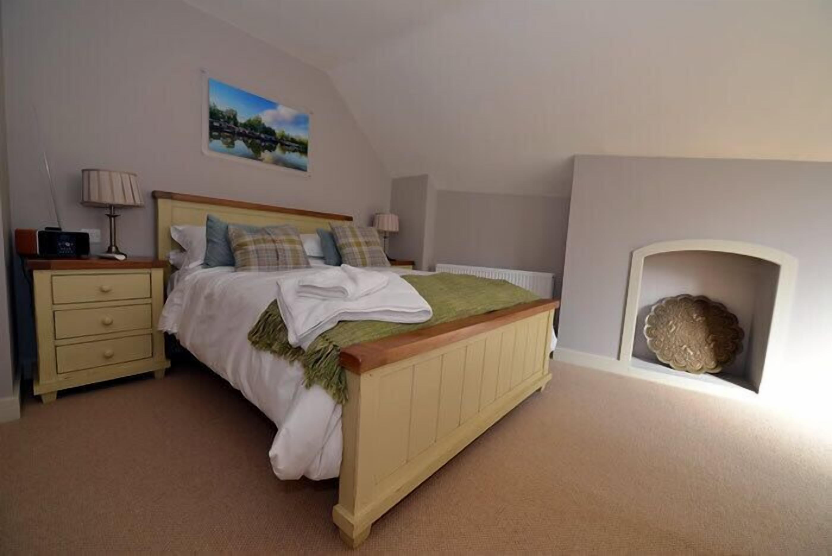 A bedroom with a bed, bedside tables, a lamp, a painting, and a fireplace.