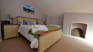 A bedroom with a bed, bedside tables, a lamp, a painting, and a fireplace.