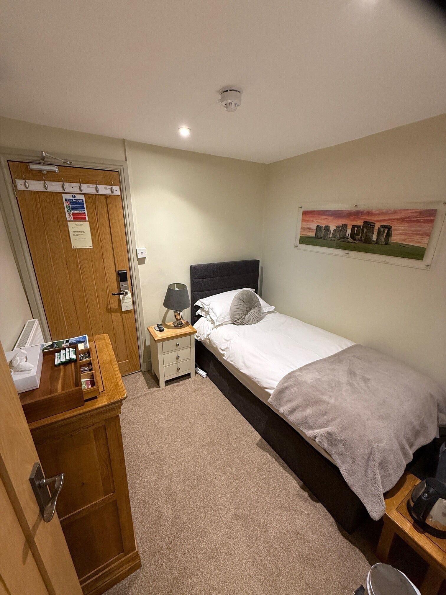 A bedroom with a bed, bedside table, lamp, and a painting on the wall.