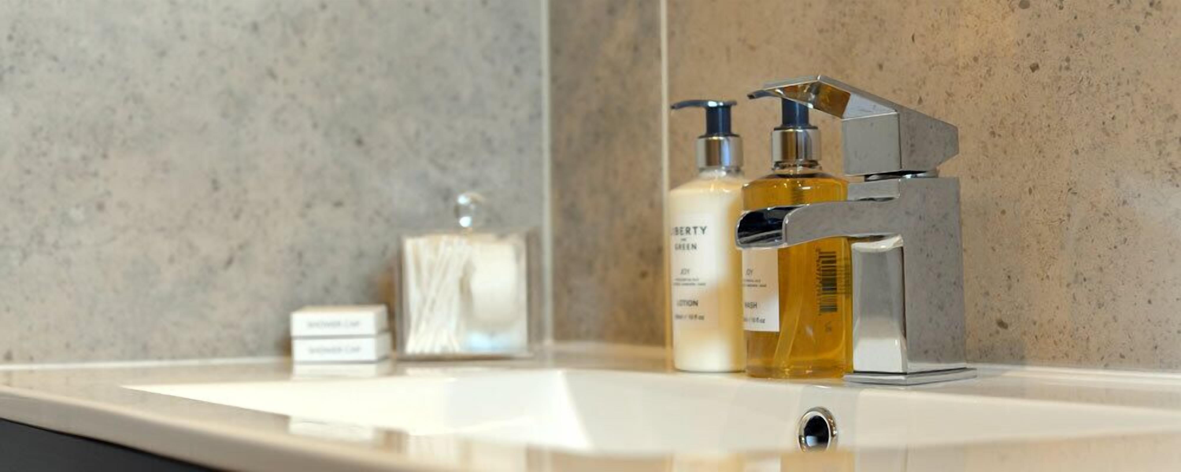 Une salle de bain avec un lavabo blanc, deux bouteilles de savon liquide et un distributeur de savon.