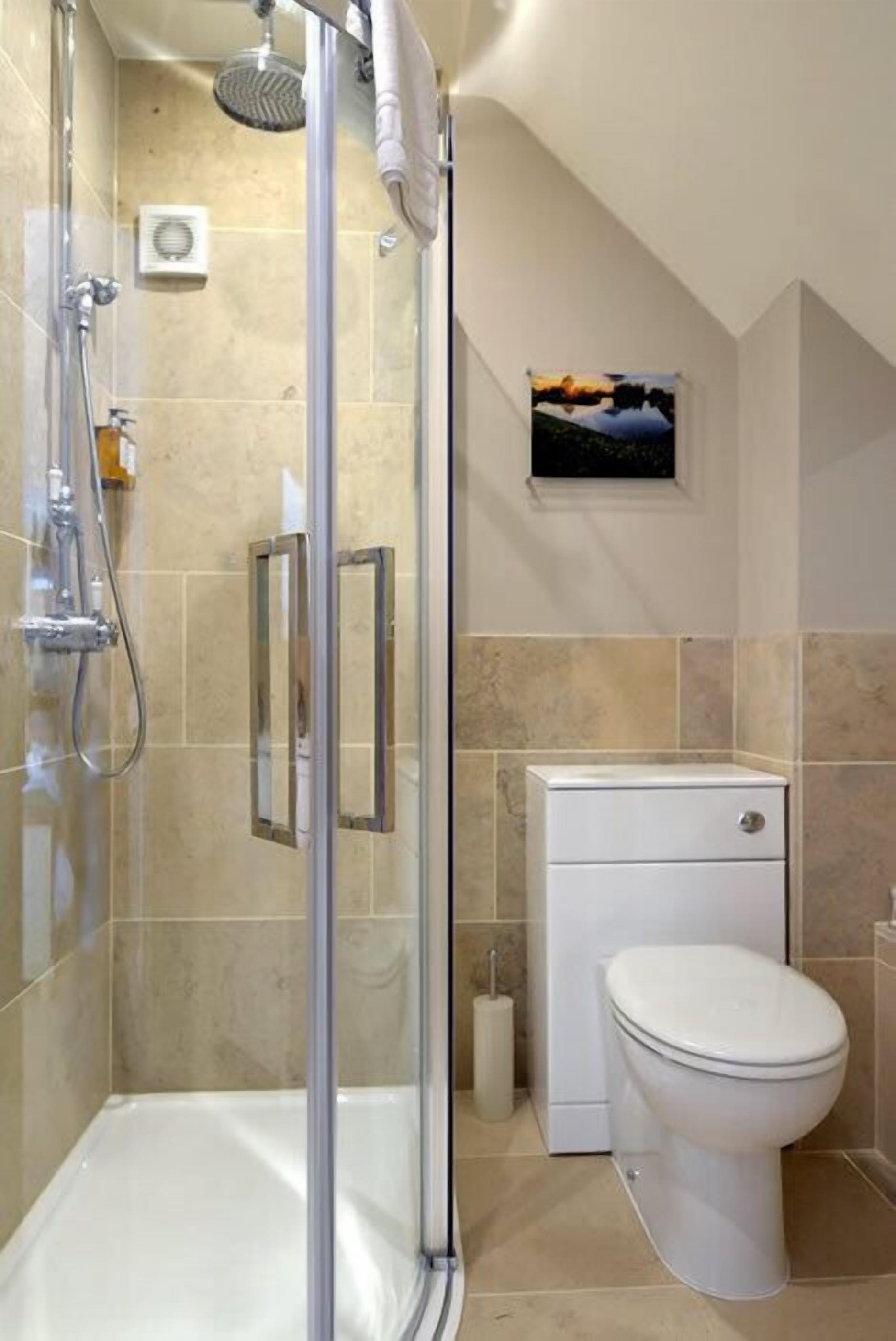 A bathroom with a glass-enclosed shower, a toilet, and a small window with a painting.