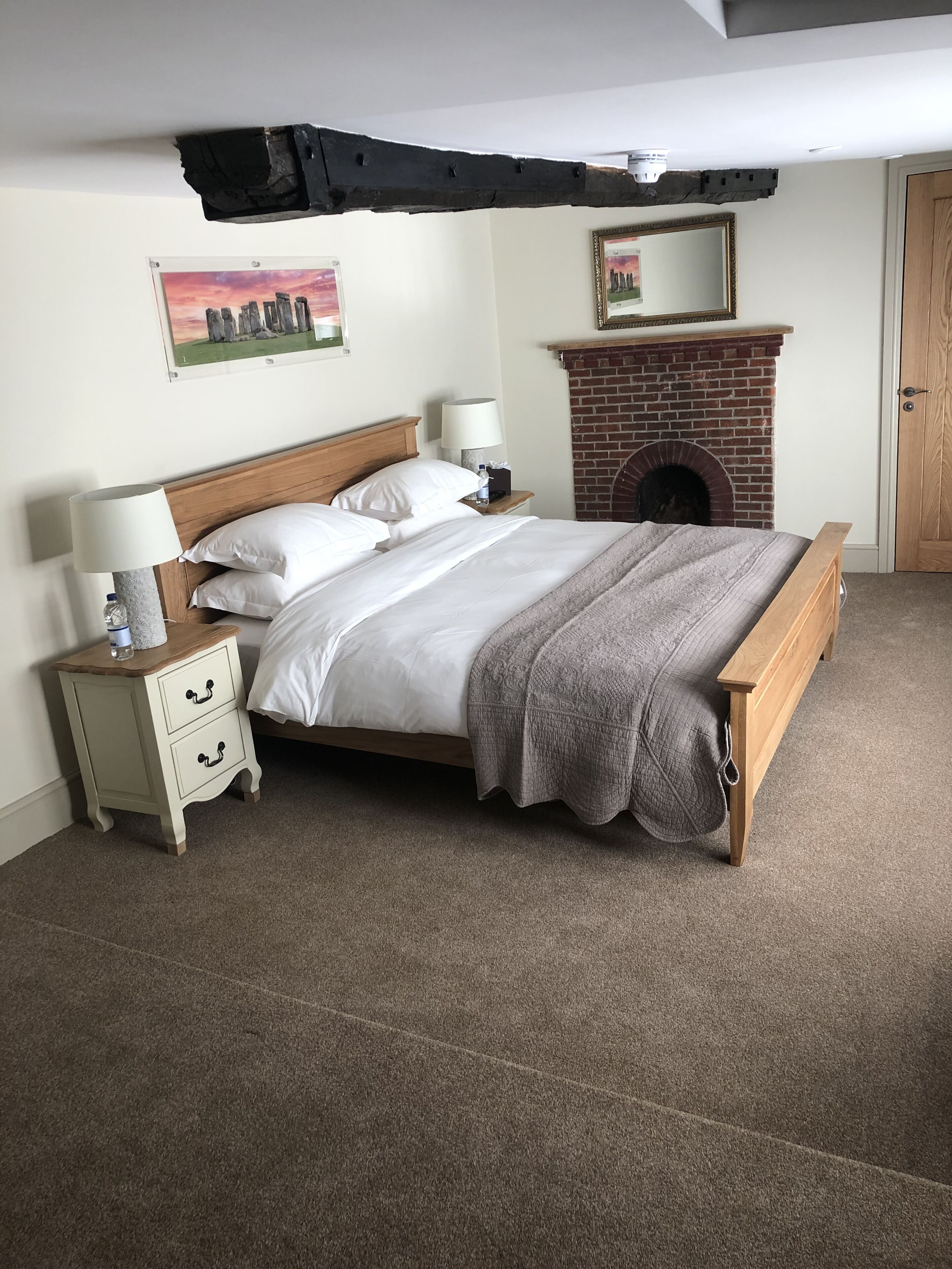 A bedroom with a bed, nightstands, a lamp, a fireplace, and a framed picture on the wall.