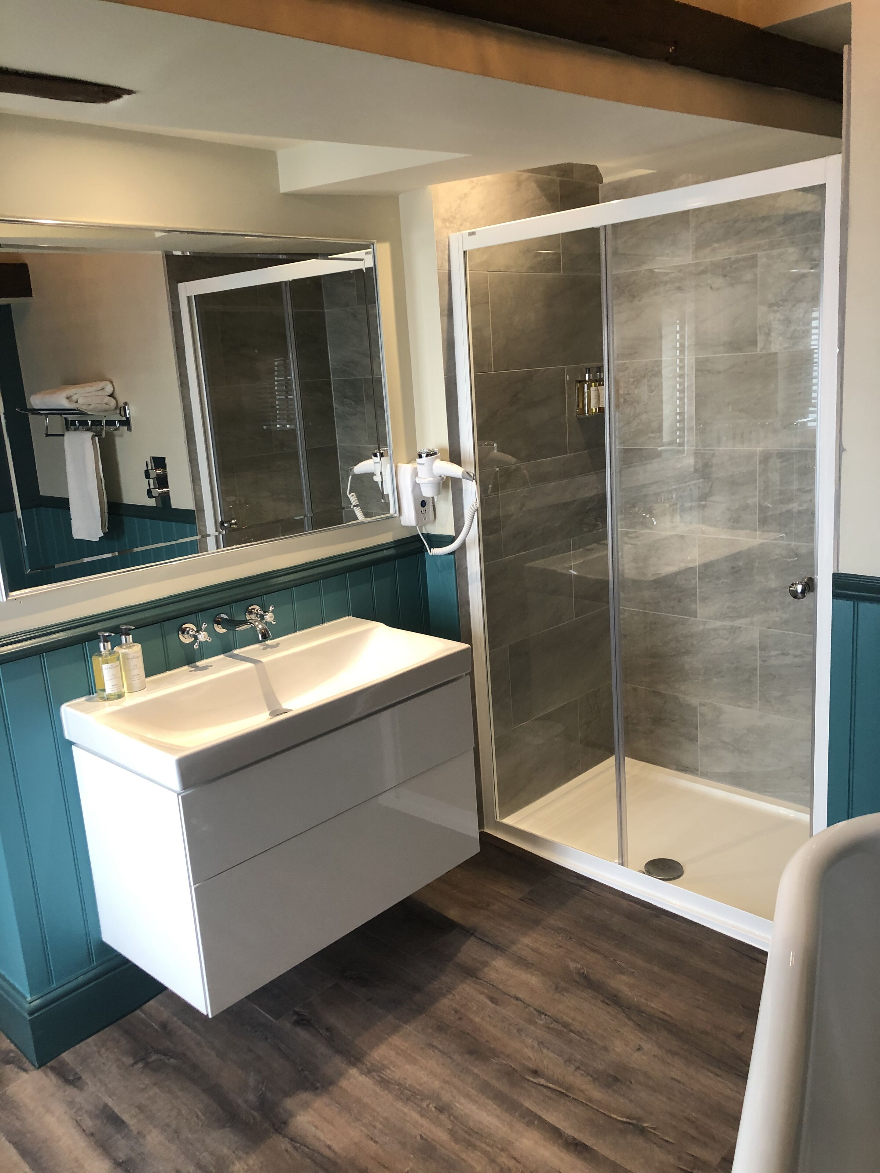Een moderne badkamer met een grote spiegel, een witte wastafel, een douchecabine en blauwgroene kastjes.