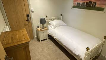 Un dormitorio con una cama individual, una mesita de noche, un aparador de madera y un cuadro en la pared.