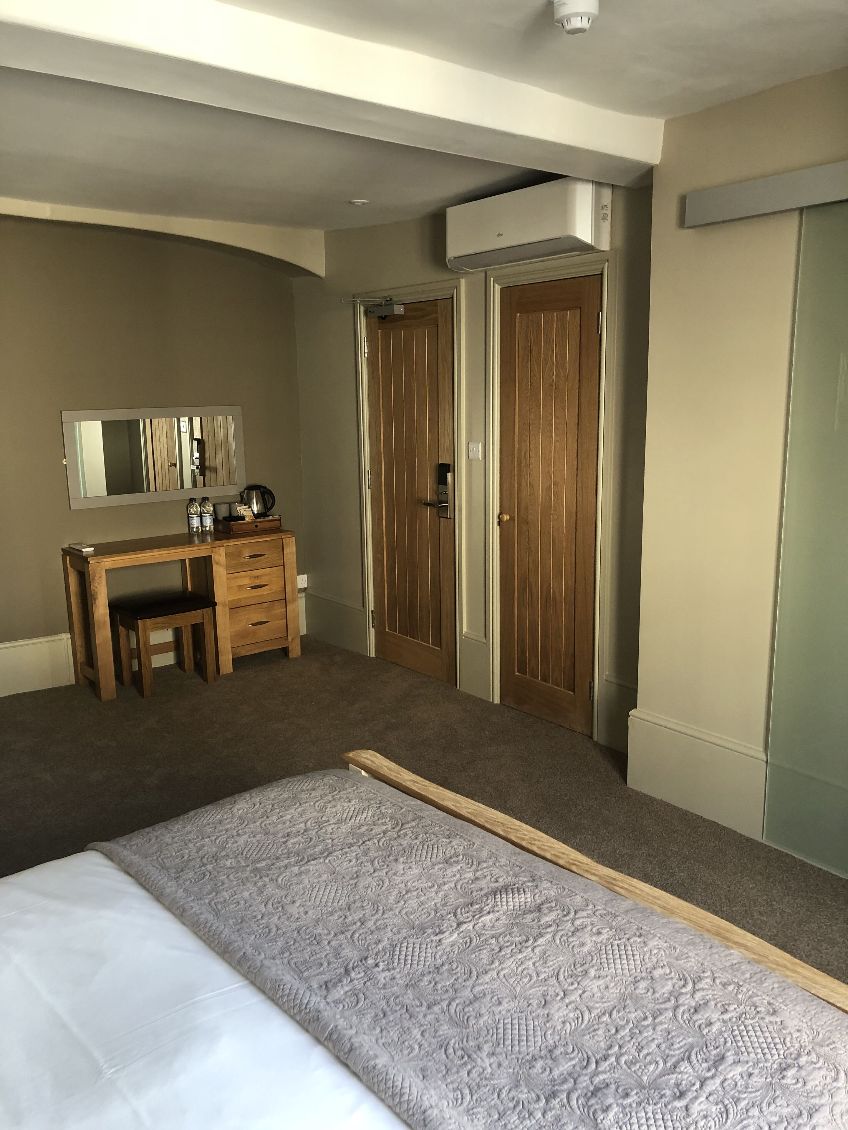 Un dormitorio con cama, escritorio, silla, espejo y dos puertas.