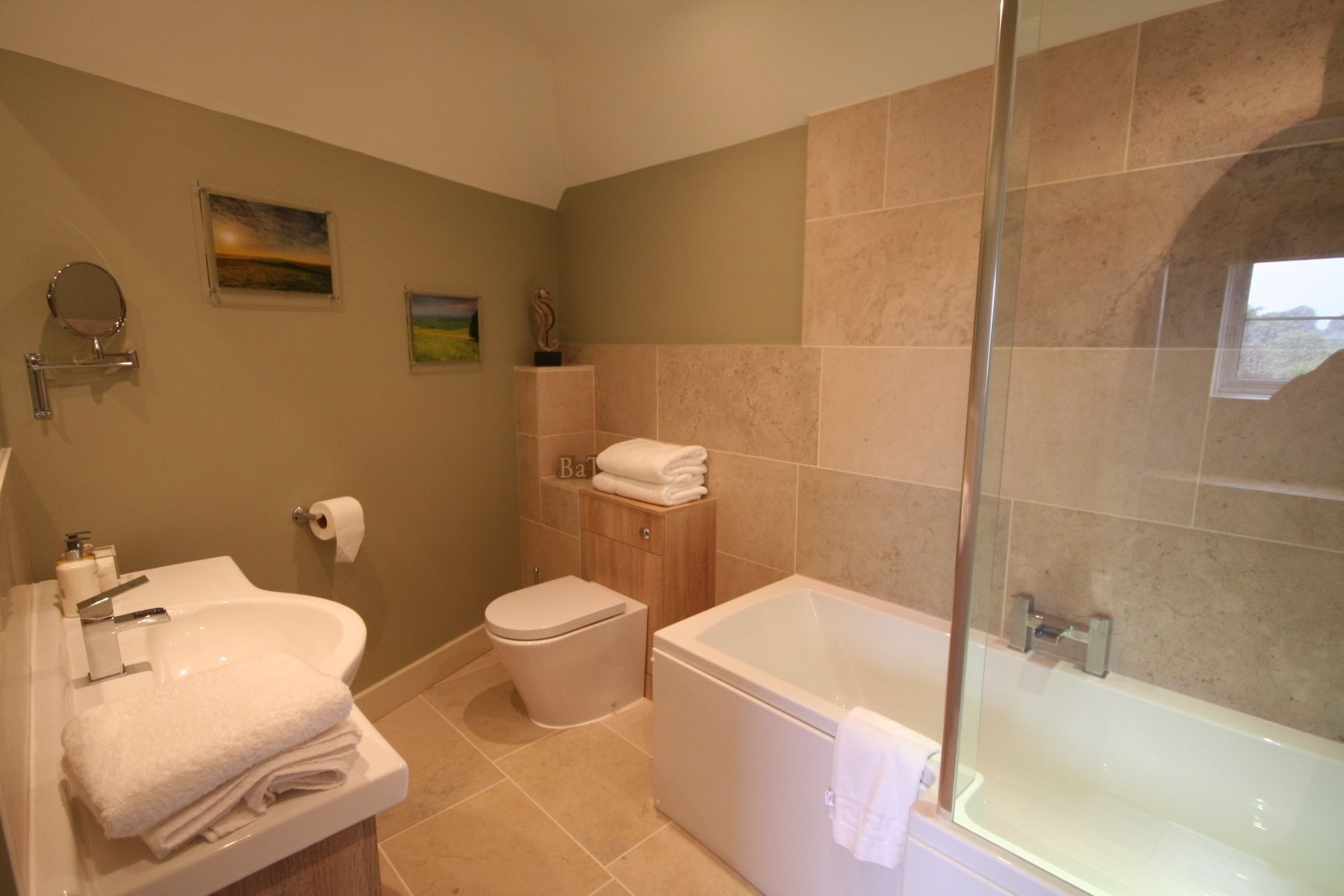 A bathroom with a bathtub, toilet, and sink. There are towels stacked on the sink and a glass shower enclosure.