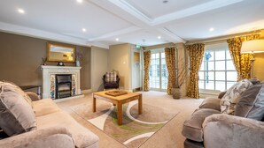 A spacious living room with a fireplace, comfortable seating, and a large window with curtains. - The Peppermill (Devizes)