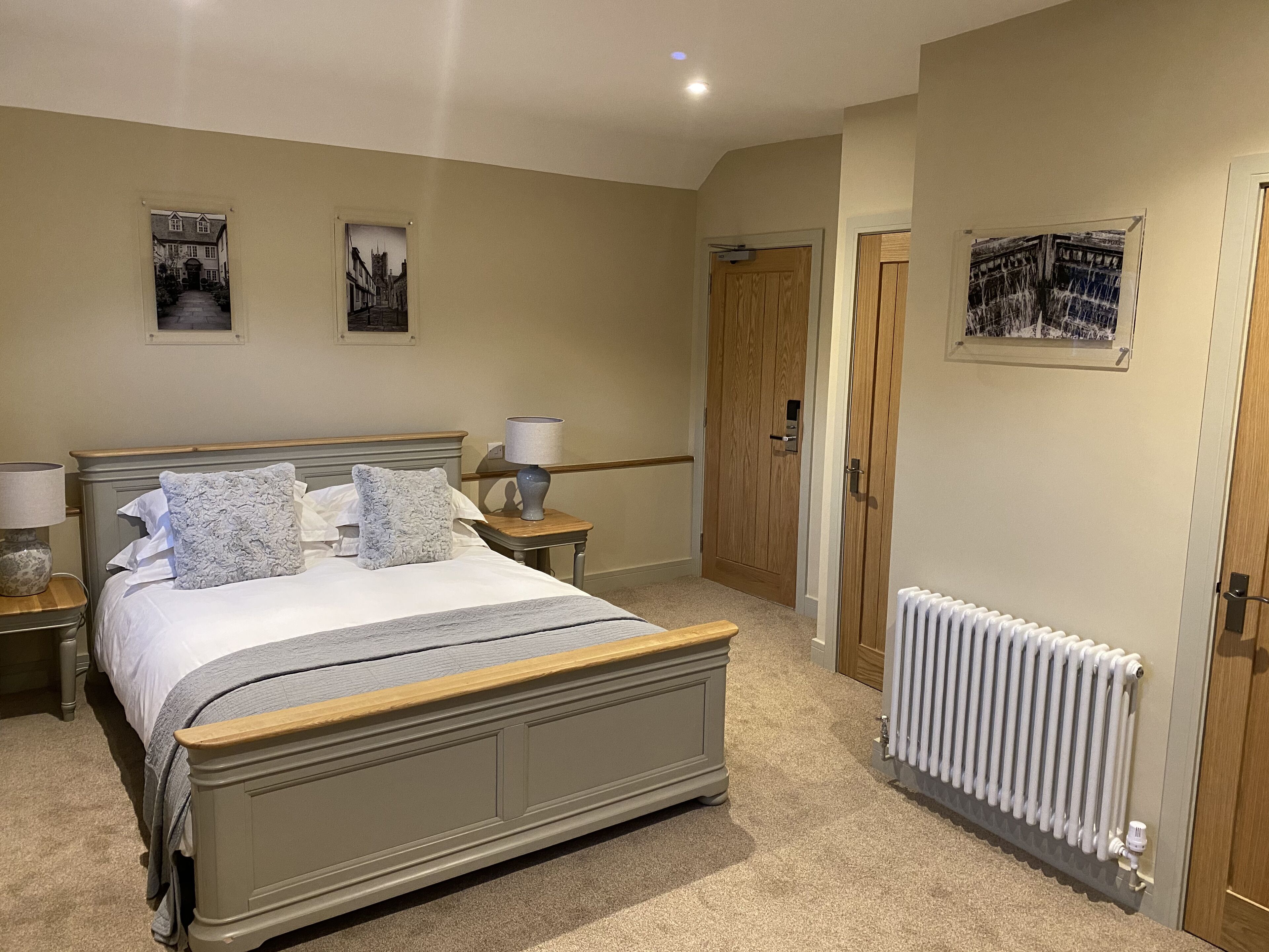 Une chambre à coucher bien rangée, avec un grand lit, des tables de chevet avec des lampes, un radiateur et des tableaux encadrés accrochés aux murs.