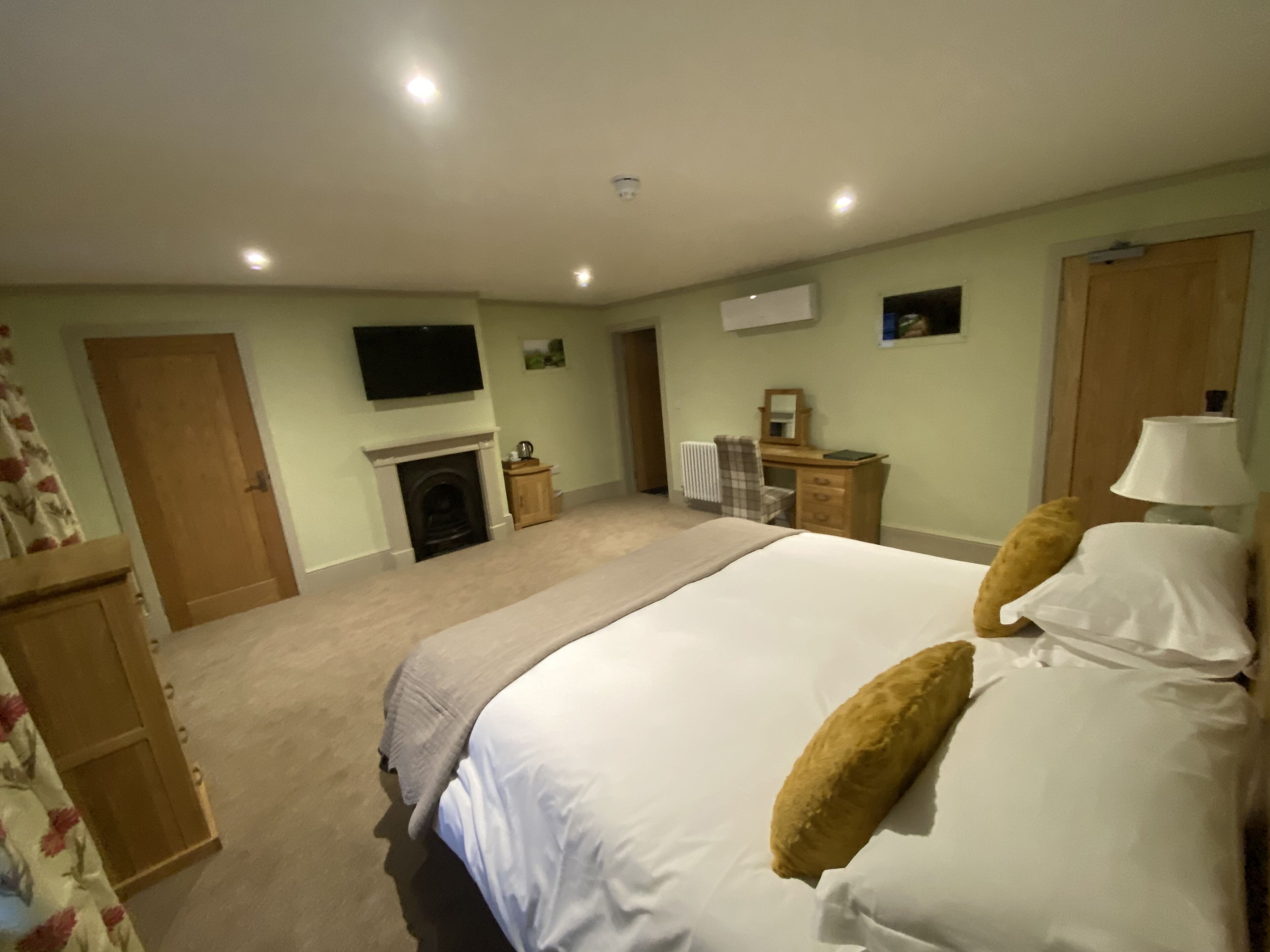 A bedroom with a bed, a dresser, a mirror, a fireplace, and a television on the wall.