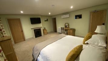 A bedroom with a bed, a dresser, a mirror, a fireplace, and a television on the wall.