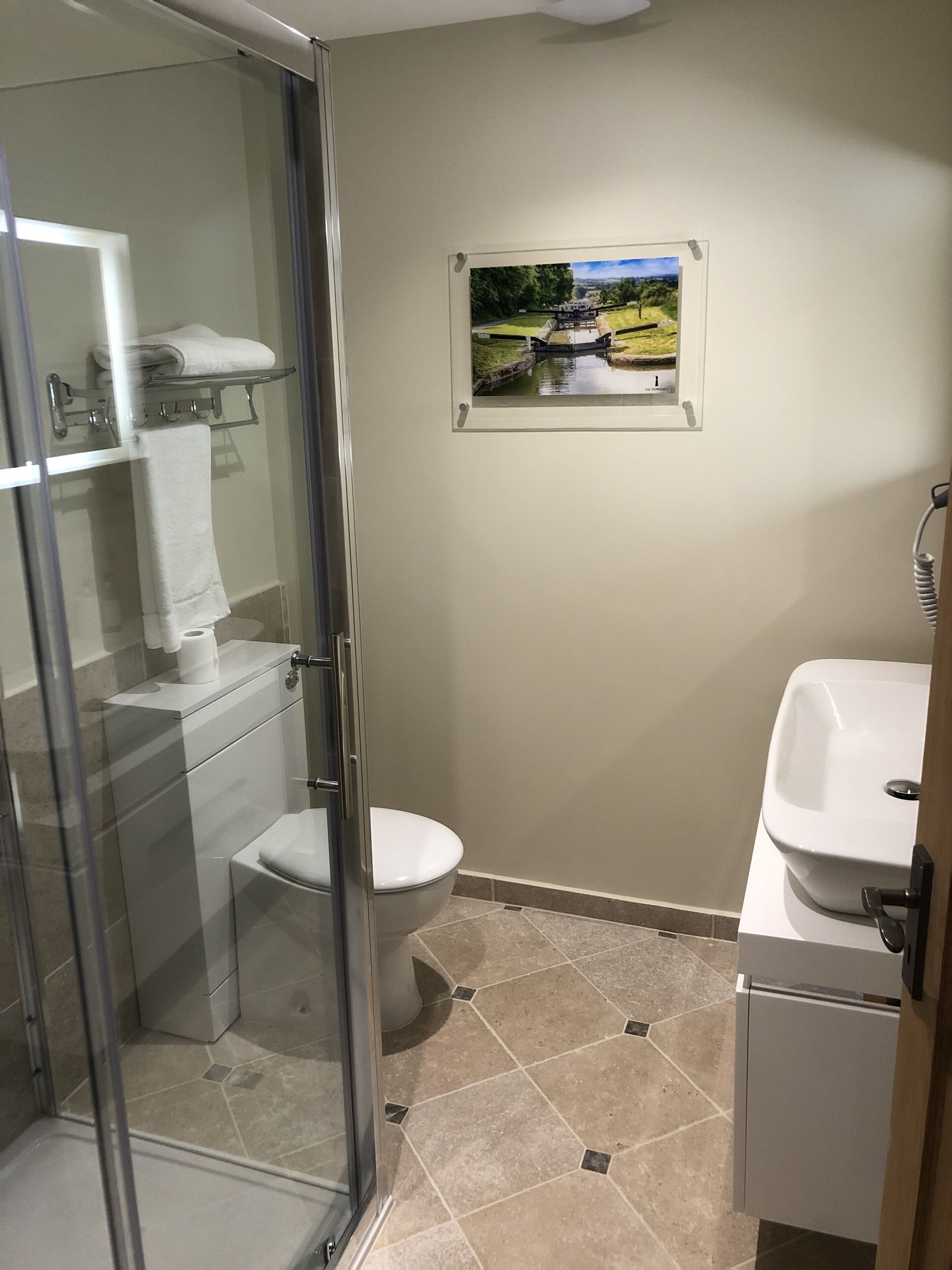 A bathroom with a glass shower enclosure, a toilet, a sink, and a framed picture on the wall.