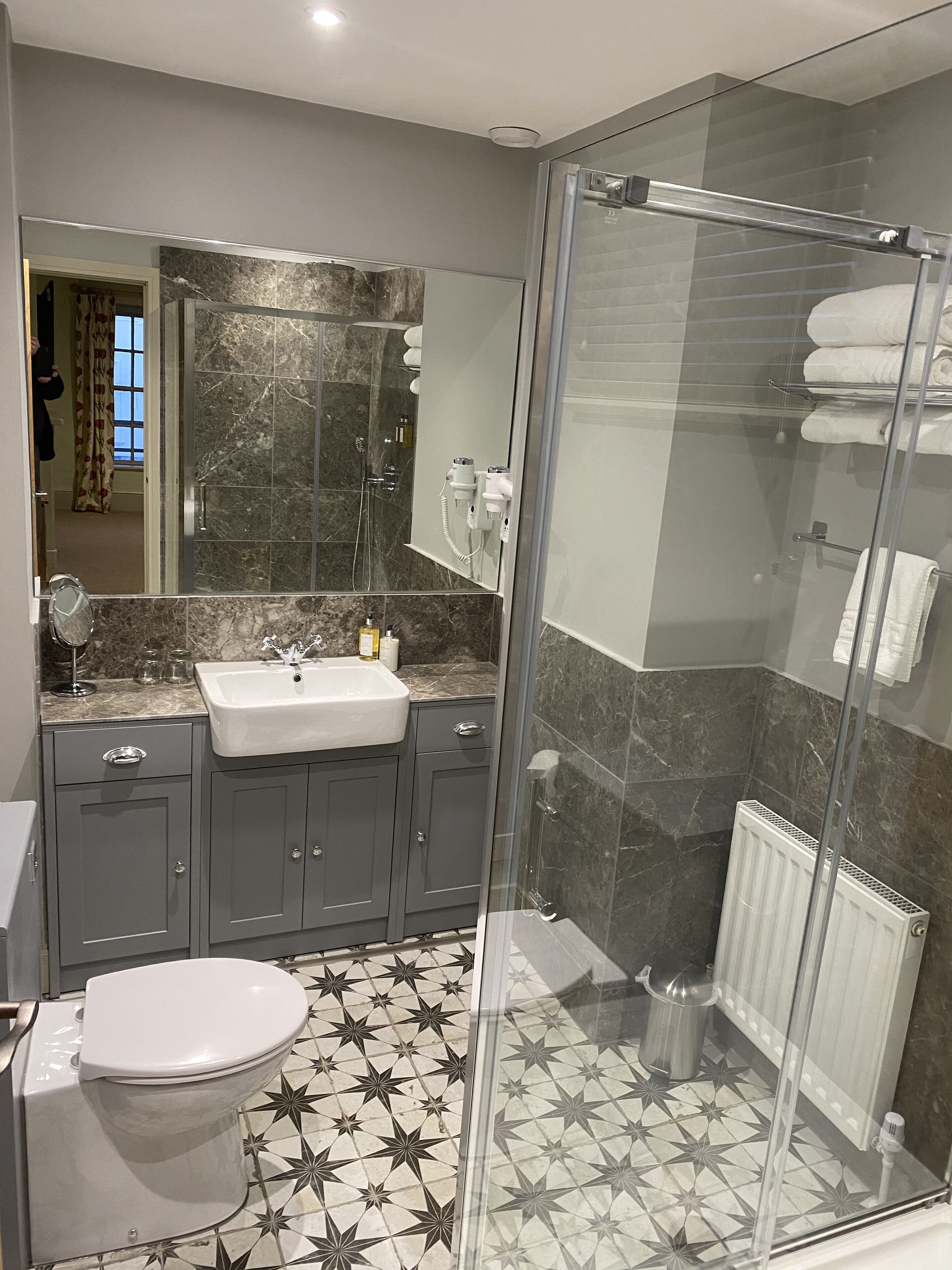 Un baño moderno con ducha de vidrio, piso de mármol y un espejo grande sobre el lavamanos.