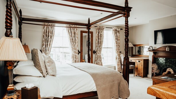 A four-poster bed with a wooden frame, a bedside table with a lamp, and a television mounted on the wall. - The Peppermill (Devizes)