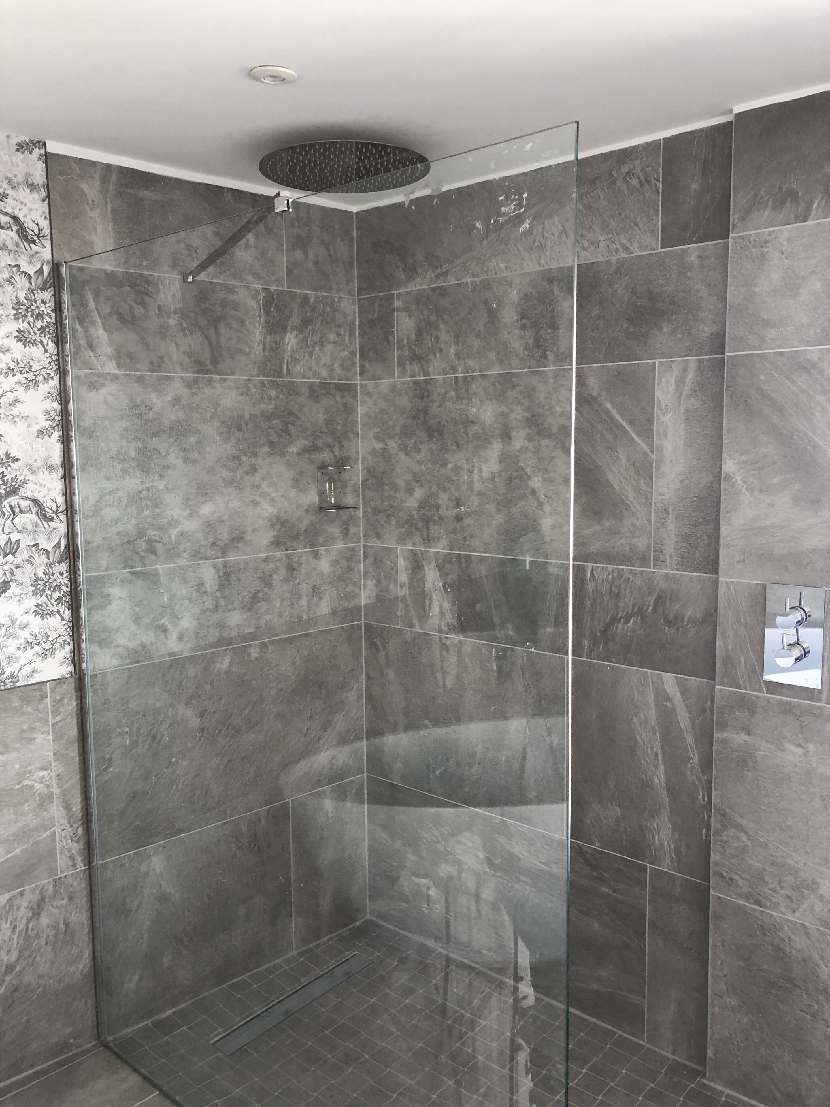Un box de ducha moderno con puerta de vidrio, azulejos de mármol gris y ducha empotrada en el techo.