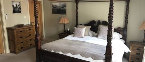 Un lit à baldaquin avec une courtepointe, une commode en bois, une table de chevet avec une lampe et un climatiseur fixé au mur.