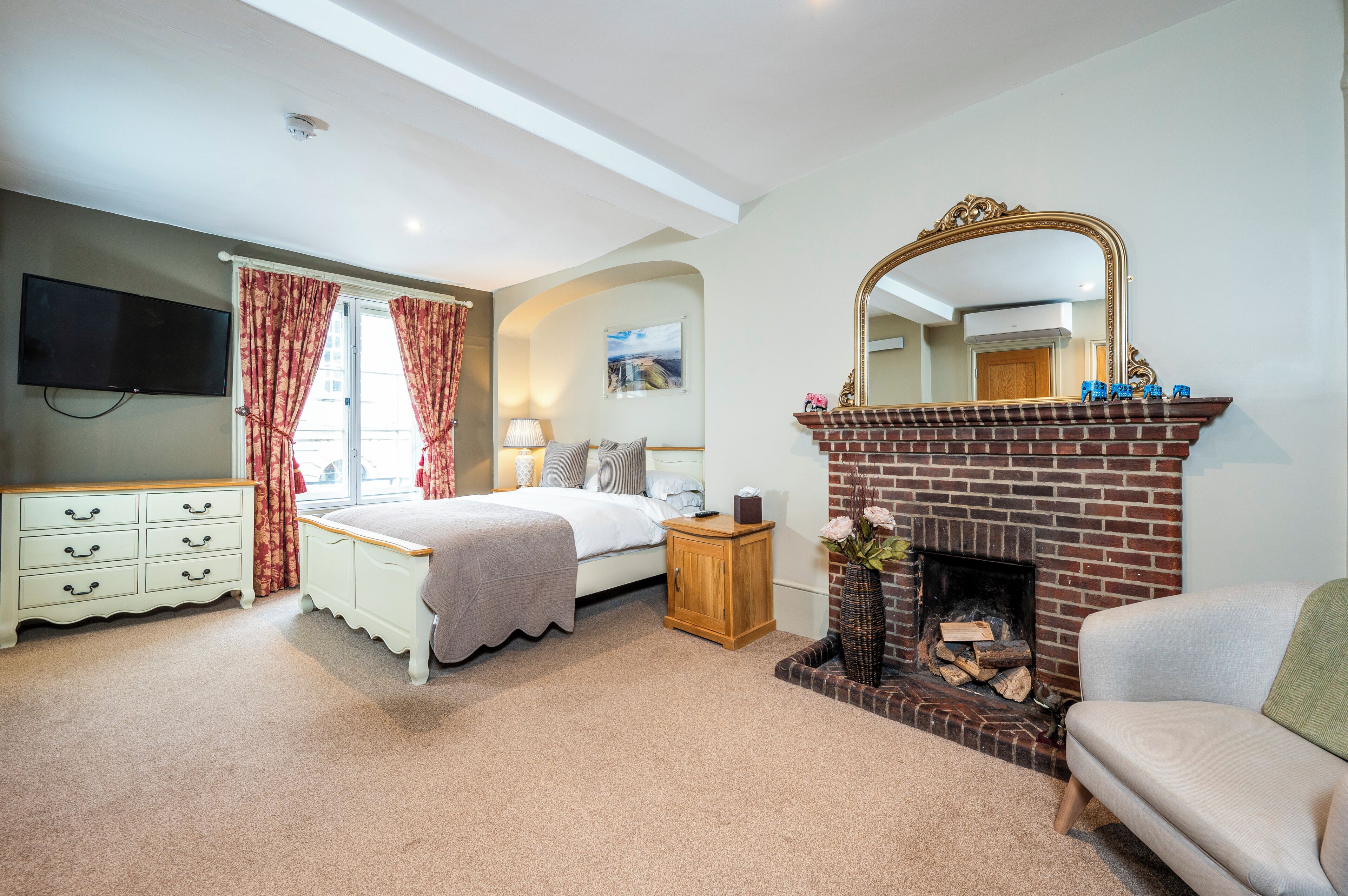 A bedroom with a bed, dresser, nightstand, fireplace, and a television.
