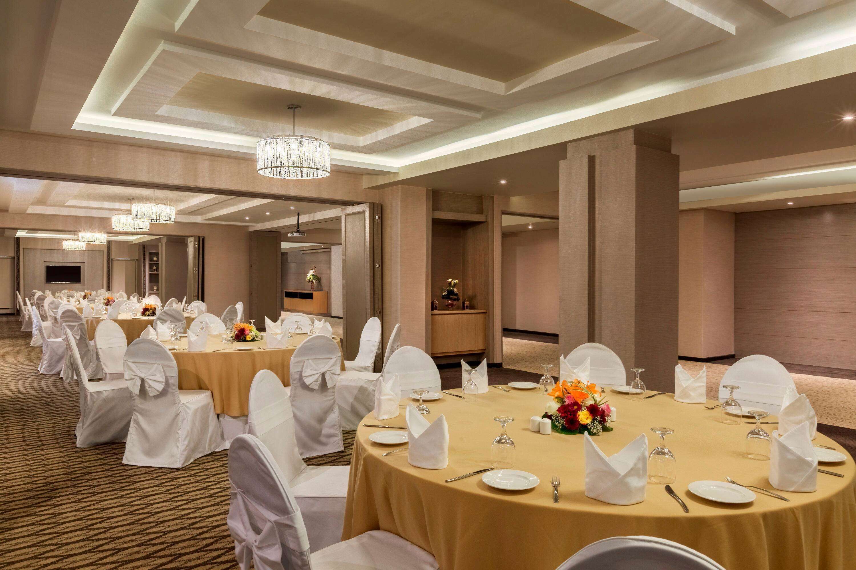 A banquet hall with round tables, white chairs, and chandeliers.