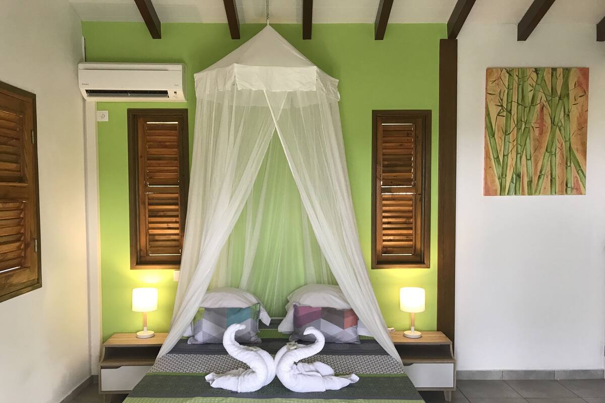 A neatly made bed with a canopy, two bedside lamps, and a wall painting.