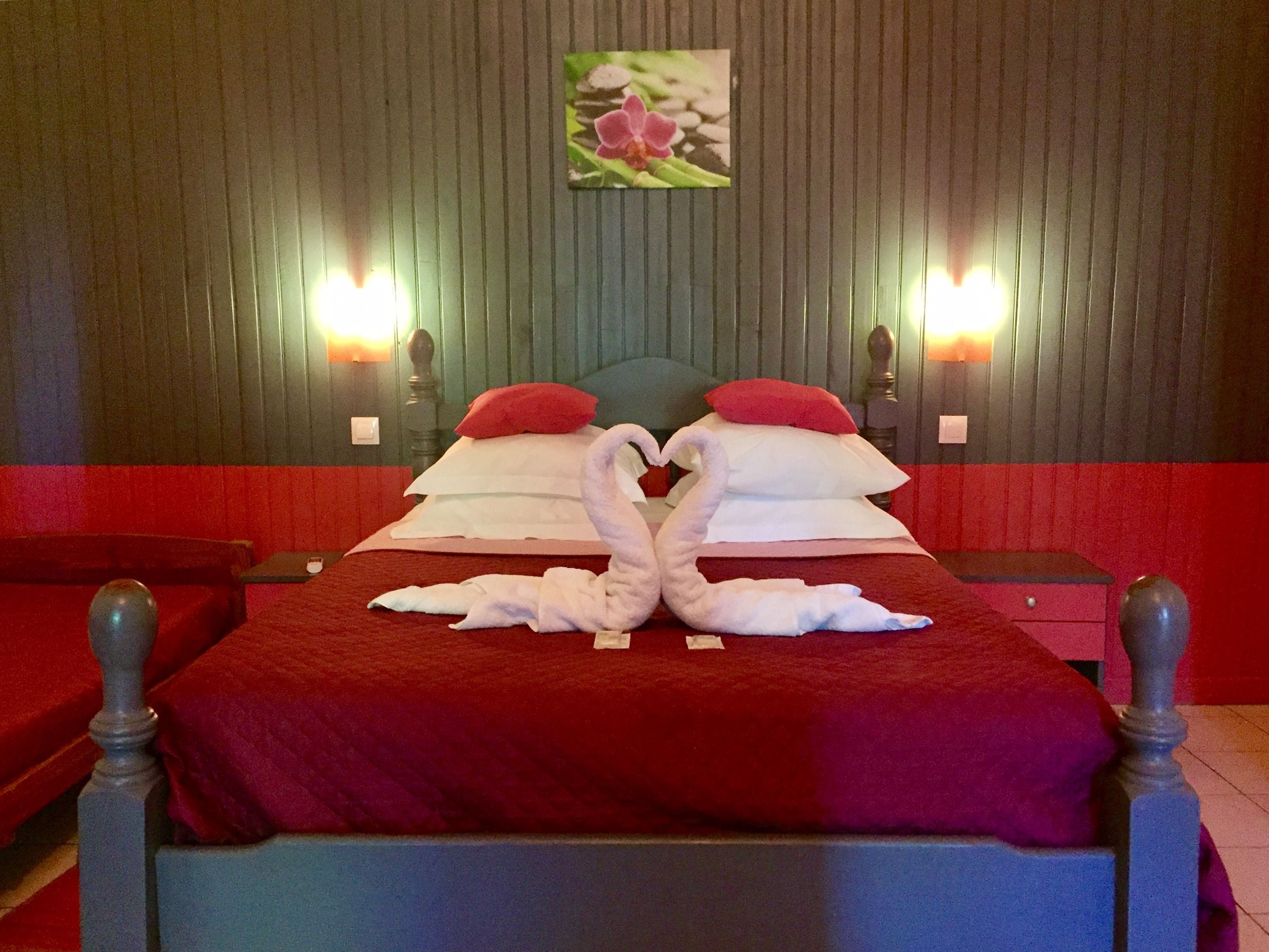 A hotel room with a bed, red and white bedding, two bedside tables, and a red sofa.