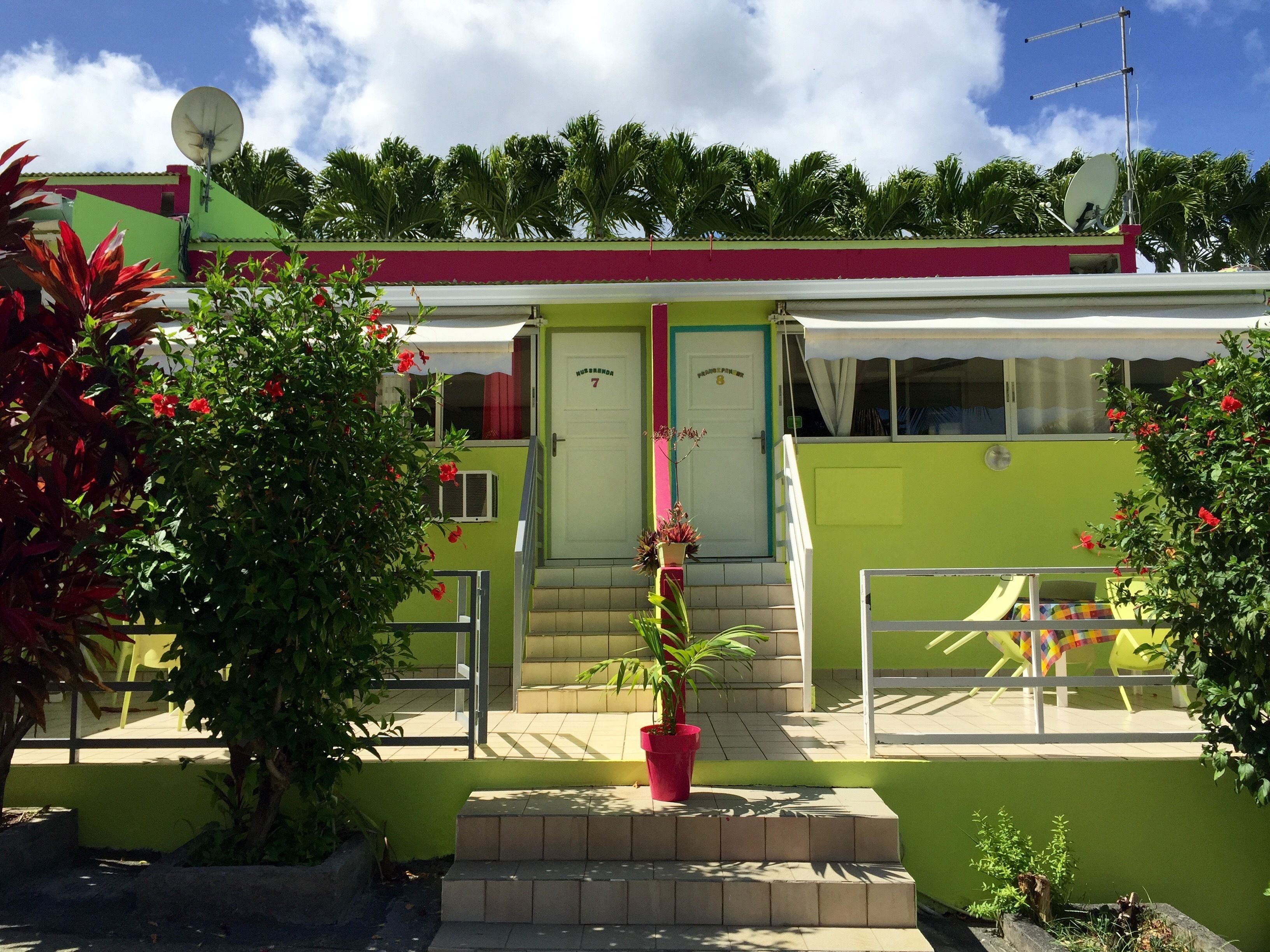 Un edificio de dos pisos con fachada verde, una puerta blanca con un número y una antena parabólica en el techo.