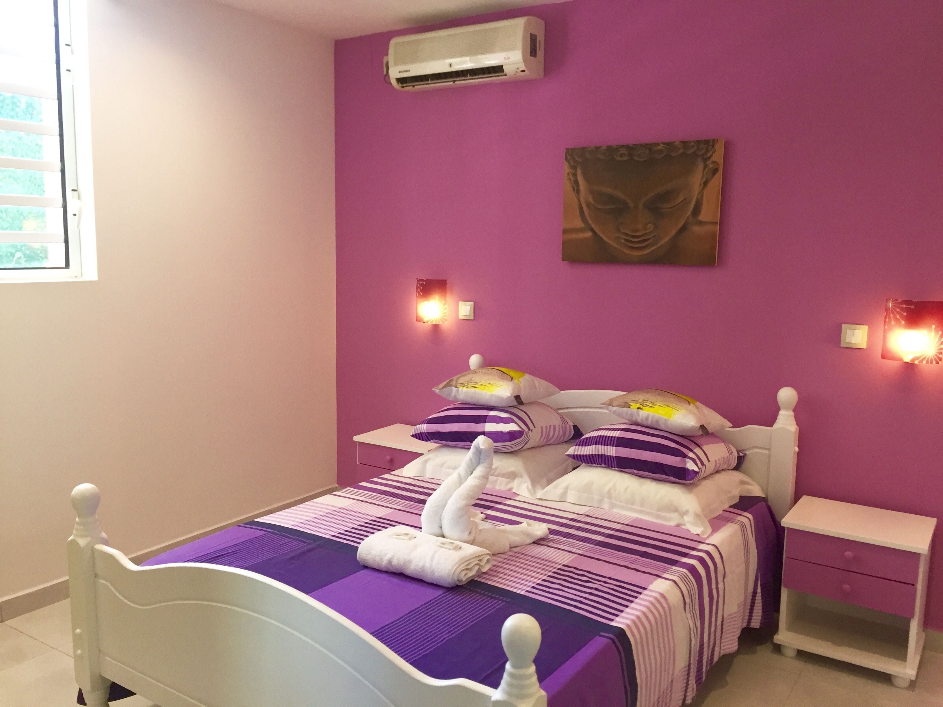 Un dormitorio con cama, mesita de noche, aire acondicionado instalado en la pared y una pintura de Buda.