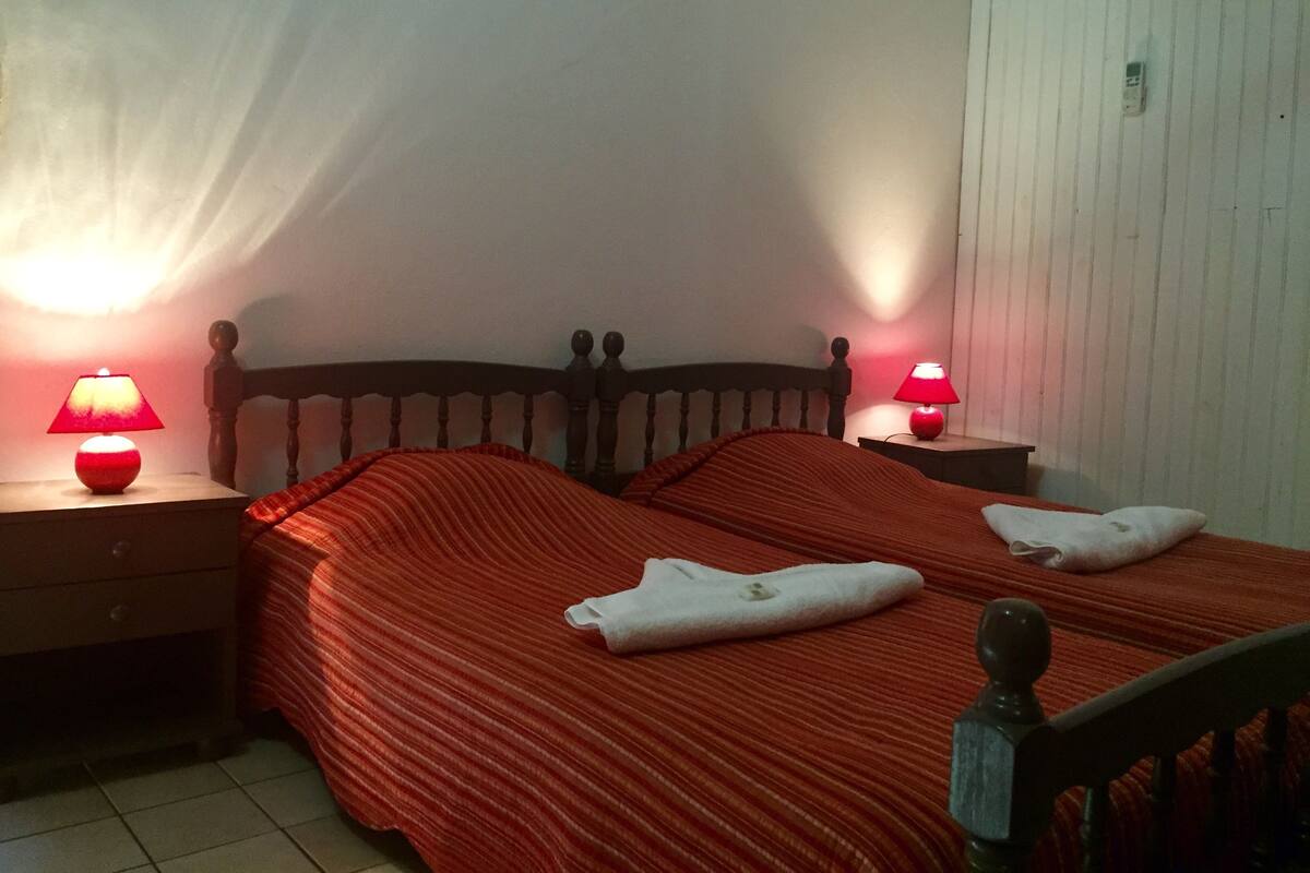 A bedroom with a wooden headboard, two bedside tables with lamps, a red striped bedspread, and two towels on the bed.
