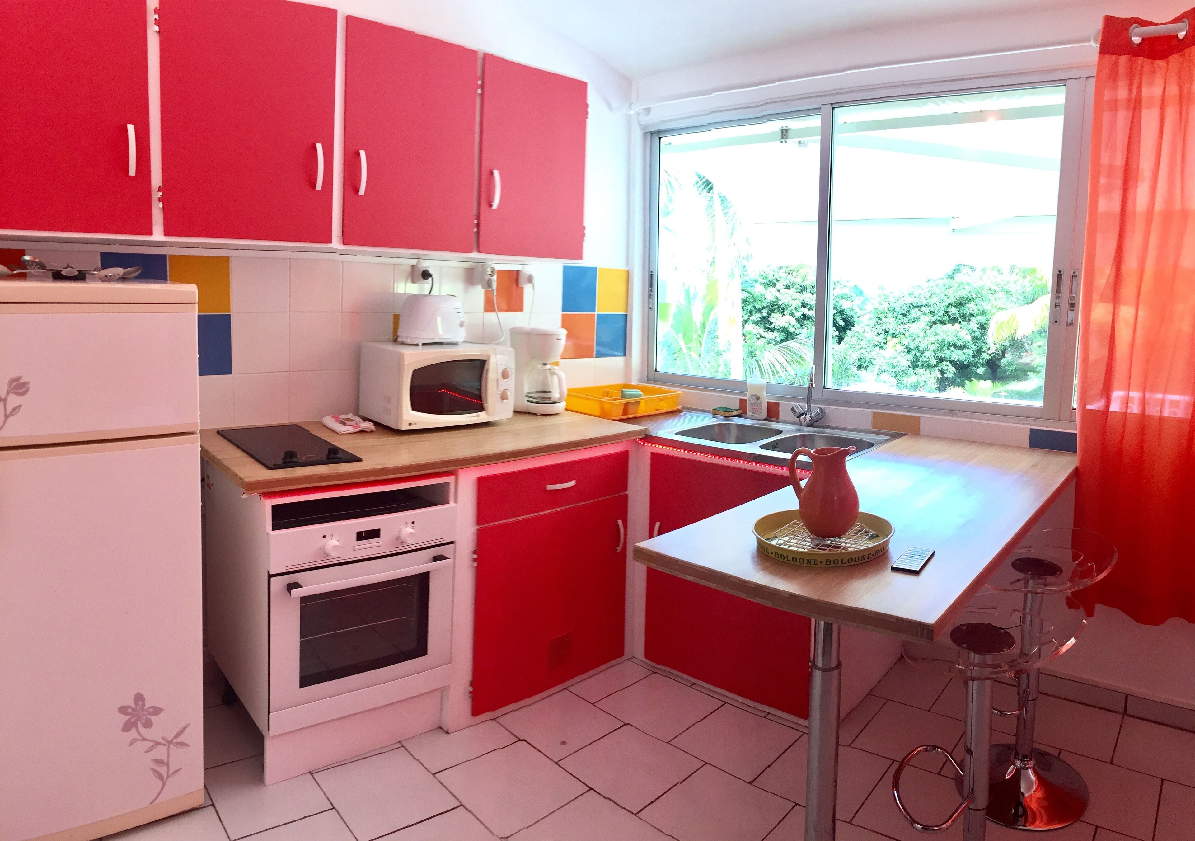Une cuisine avec des meubles de couleur rouge, un réfrigérateur blanc, un four à micro-ondes et une machine à café.