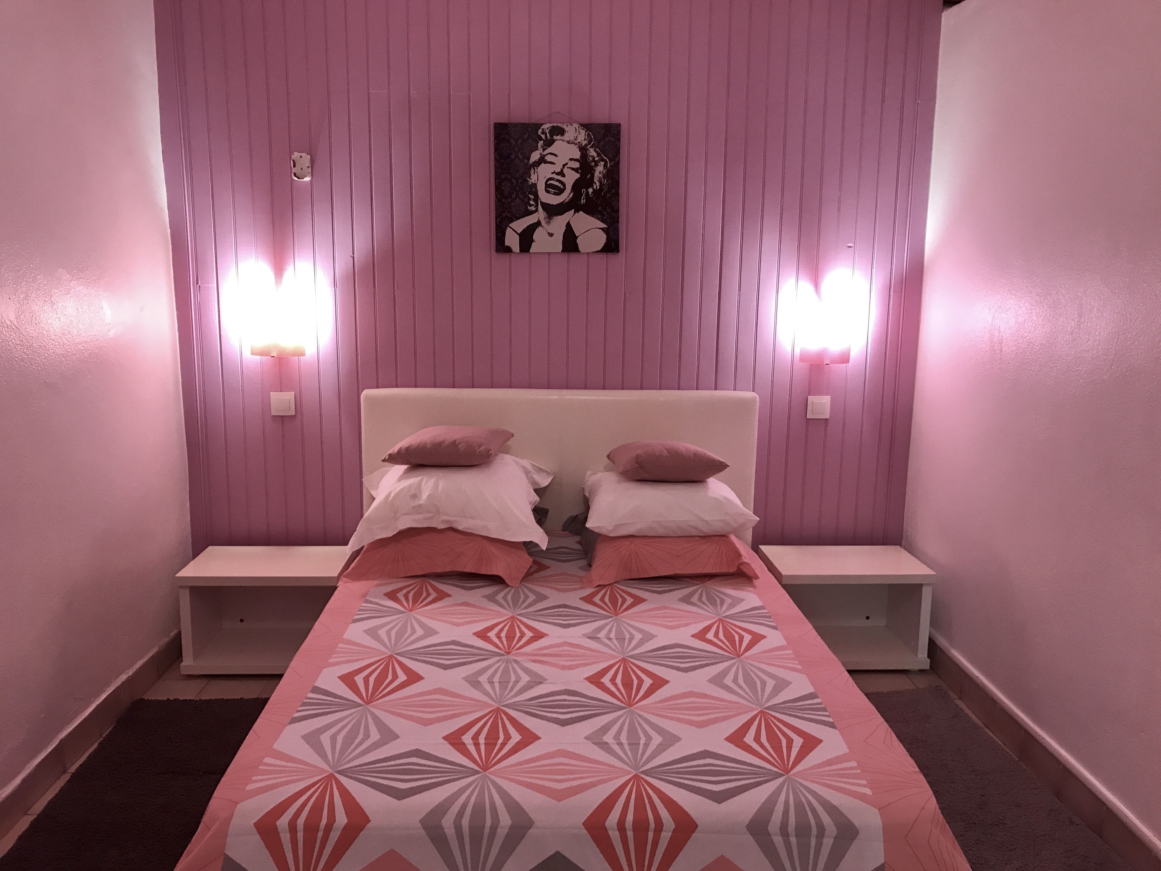 Una habitación con una cama, dos mesitas de noche y una lámpara fijada a la pared.
