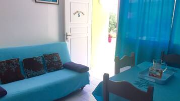 Una habitación con un sofá azul, una mesa de comedor con una jarra de vidrio y una puerta con una placa de número.