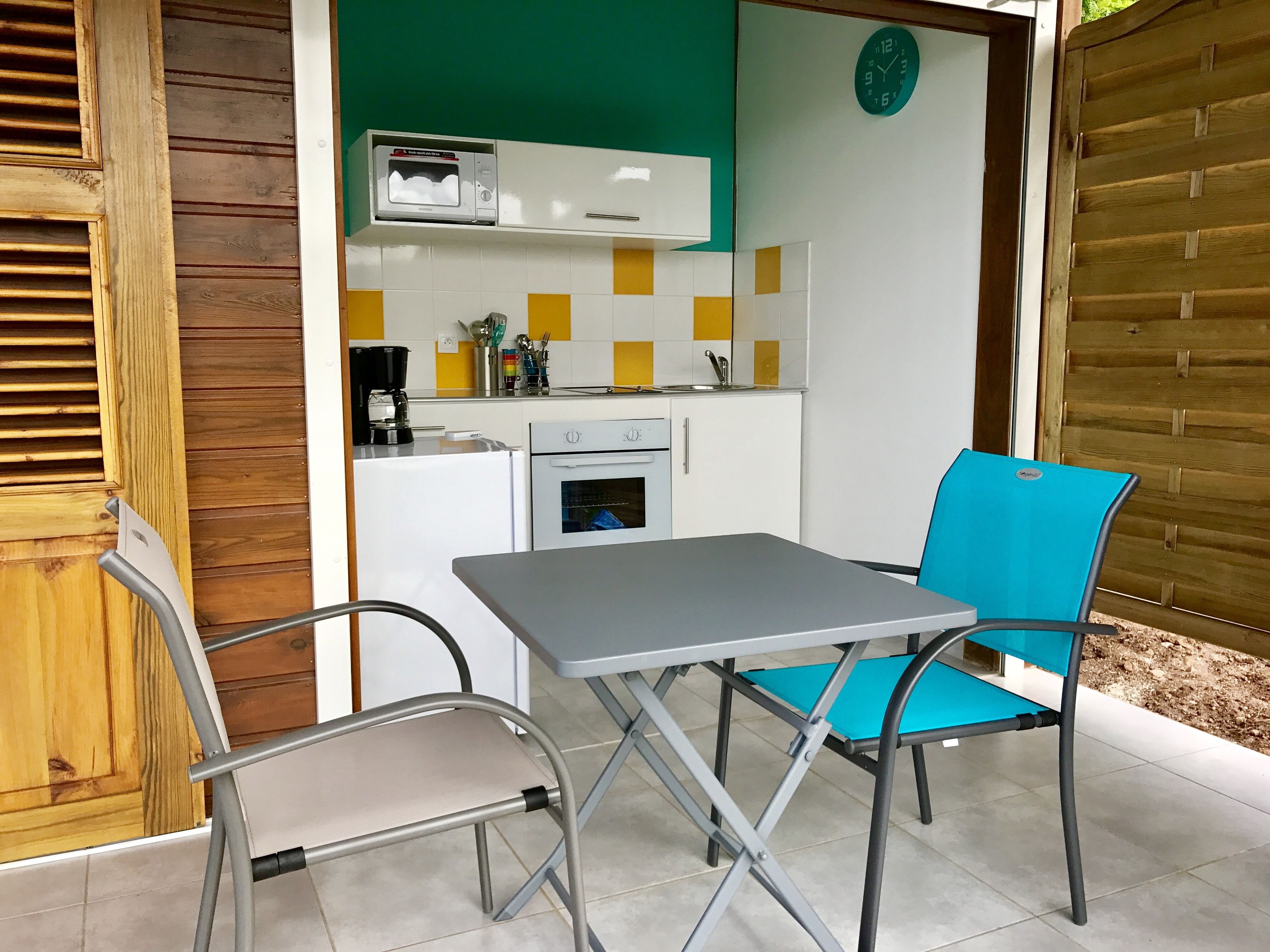 A compact kitchen with a microwave, coffee maker, and oven. There is a table with two chairs, one blue and one grey.