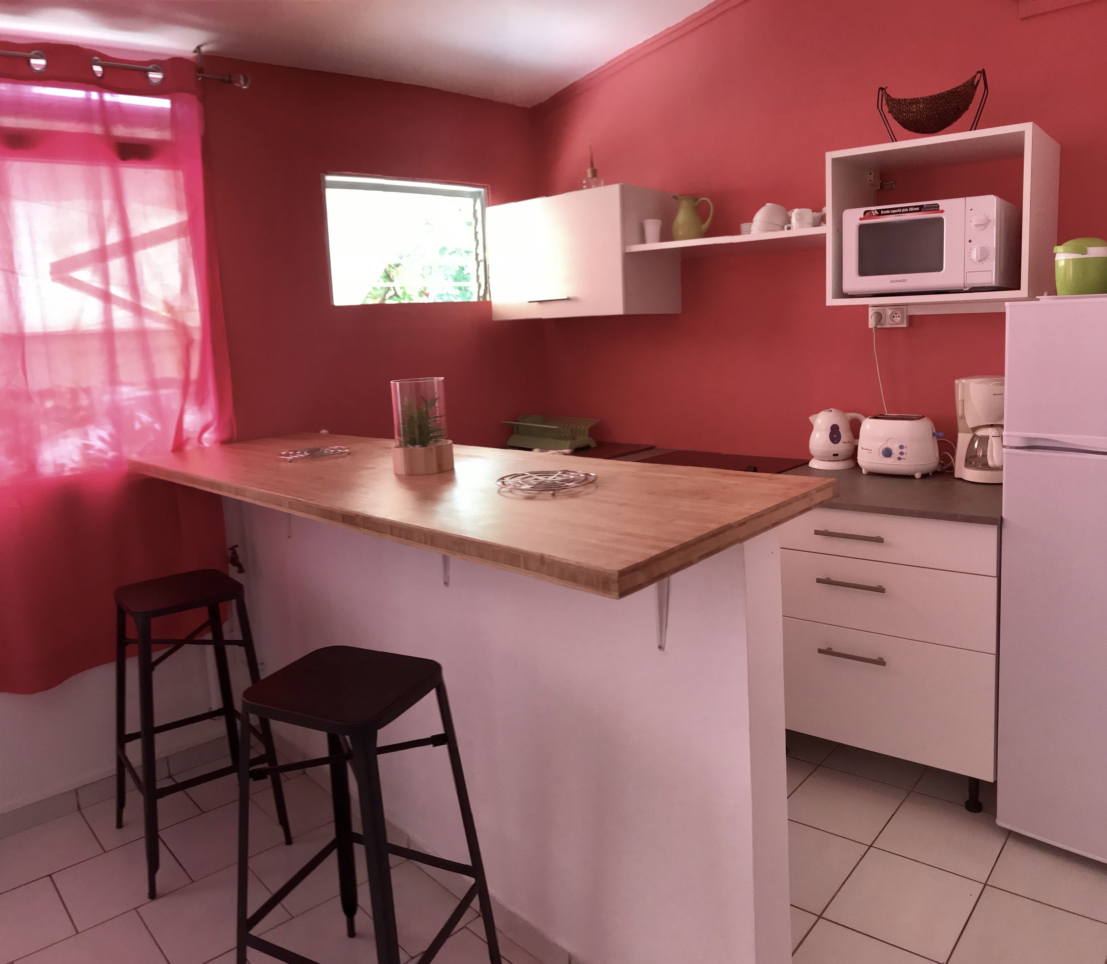 Une cuisine avec un plan de travail en bois, deux tabourets noirs, un four à micro-ondes, une machine à café et une petite étagère contenant des ustensiles de cuisine.