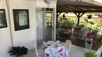 Un patio techado con mesa y sillas, plantas en macetas y vistas al exterior.