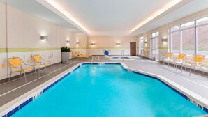 An indoor swimming pool with clear blue water, surrounded by yellow and white lounge chairs, and large windows offering a view of the outdoors. - Fairfield Inn & Suites Pittsburgh Airport/Robinson Township (Pittsburgh)