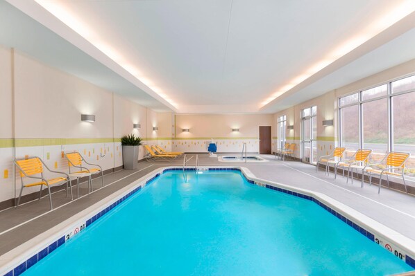 An indoor swimming pool with clear blue water, surrounded by yellow and white lounge chairs, and large windows offering a view of the outdoors. - Fairfield Inn & Suites Pittsburgh Airport/Robinson Township (Pittsburgh)