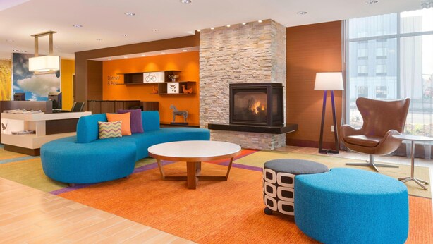 A modern living room with a stone fireplace, blue sofas, a round coffee table, and a large window offering a city view. - Fairfield Inn & Suites Pittsburgh Airport/Robinson Township (Pittsburgh)