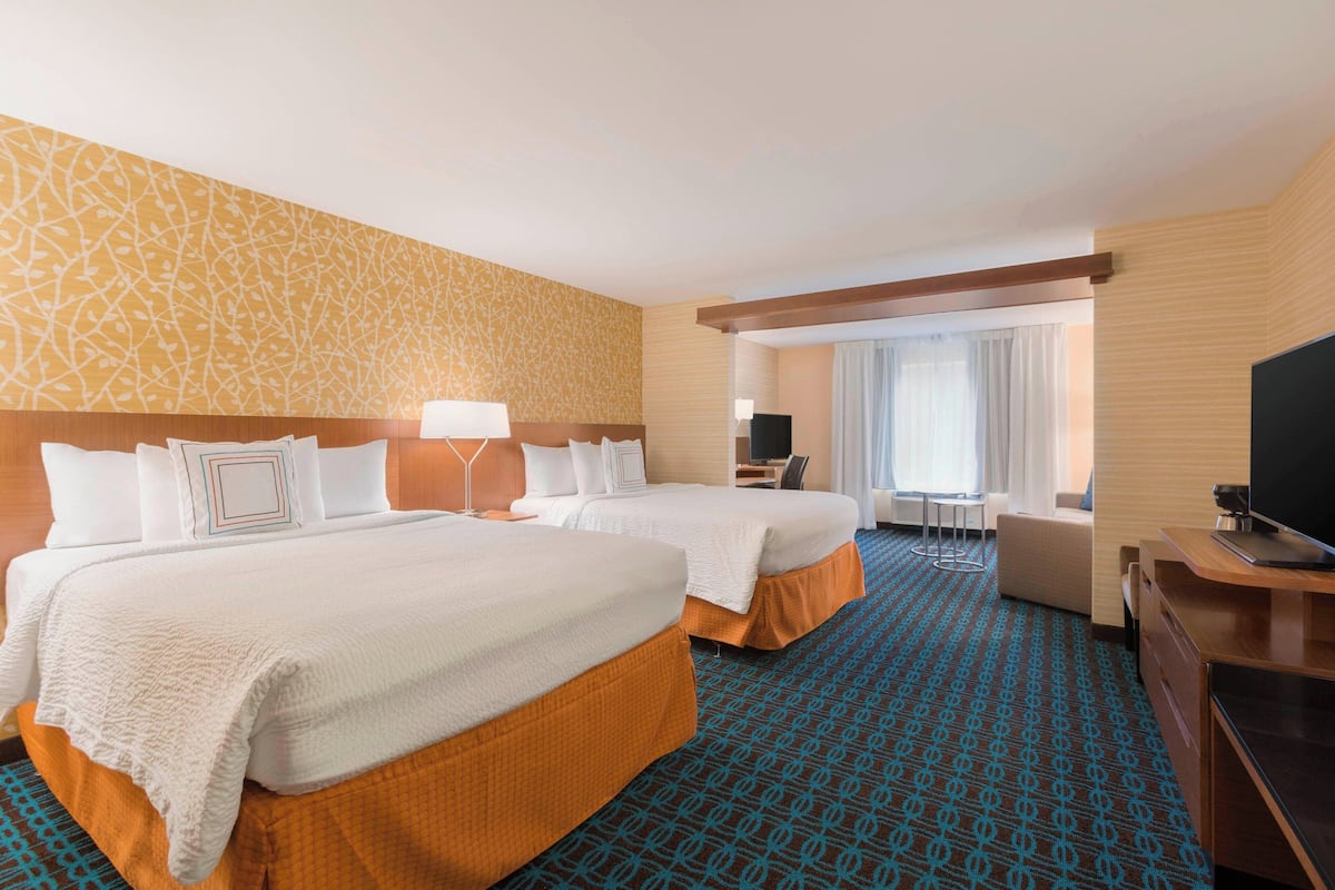 A hotel room with two beds, a desk, a chair, a TV, and a large window with curtains.